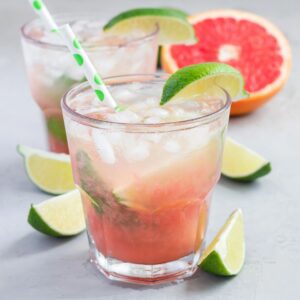Cold pink cocktail with fresh grapefruit, lime and ice cubes on concrete background, paloma, square